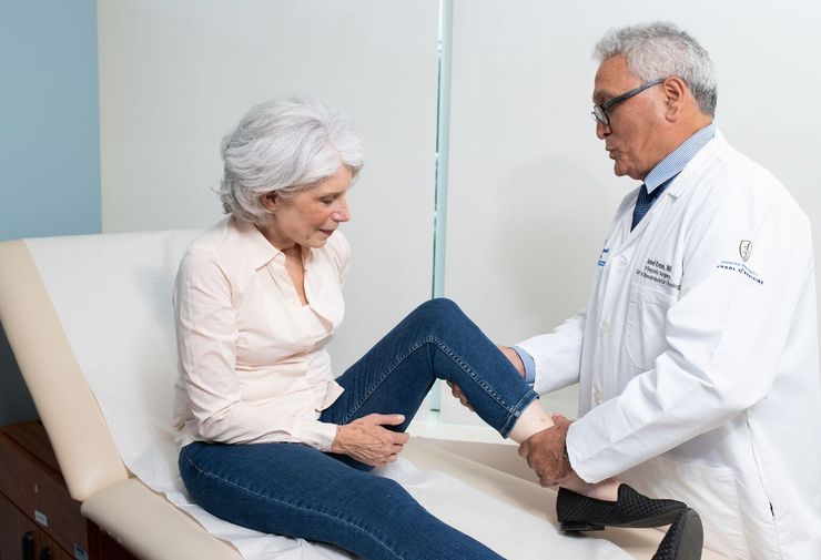 Doctor examining an older patient's ankle and foot during an orthopedic clinic visit