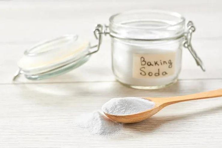 Glass jar labeled Baking Soda with a wooden spoon full of white powder on a kitchen counter