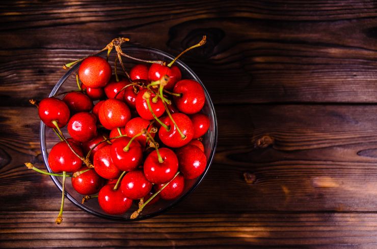 Glass bowl full of fresh red cherries on a dark wooden table