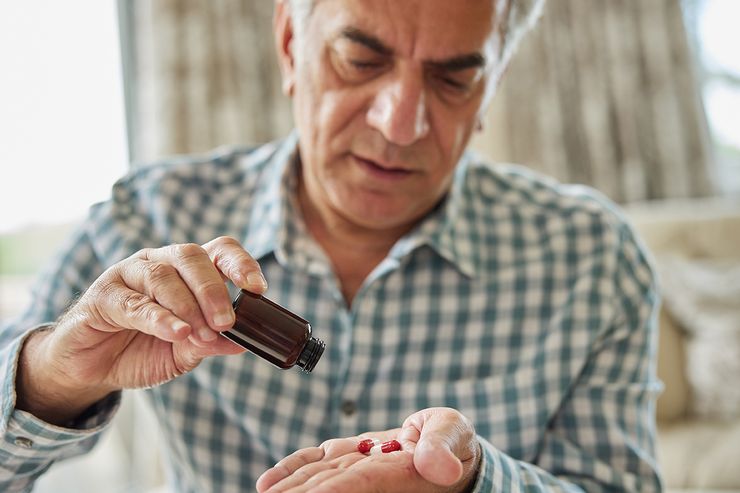 Middle-aged man pouring capsules from a brown prescription bottle into his hand at home