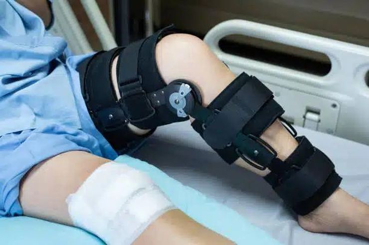 Patient resting in a hospital bed wearing a black hinged knee brace after orthopedic surgery