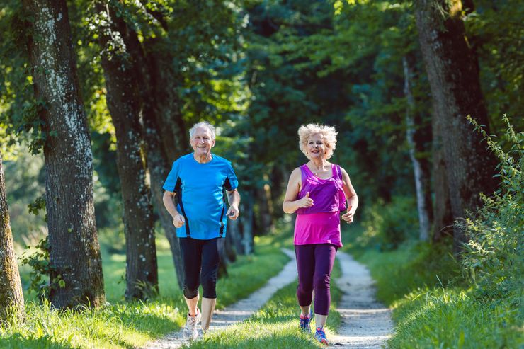 Two older adults jogging together on a wooded trail for gentle aerobic exercise