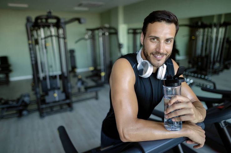 Man resting with a water shaker bottle at the gym during a workout break