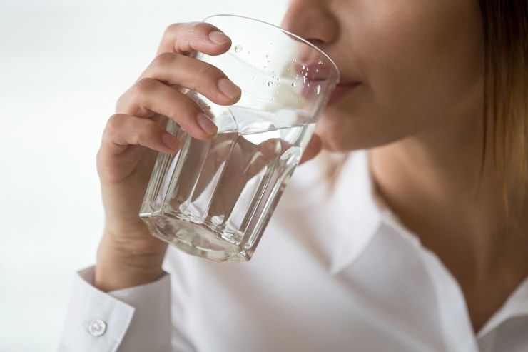 Woman drinking a glass of clear water at home, one of the few cheap habits that genuinely helps with gout