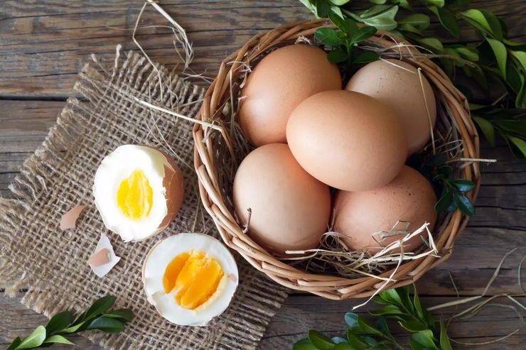 Fresh brown eggs in a wicker basket with halved hard-boiled eggs on a rustic wooden table