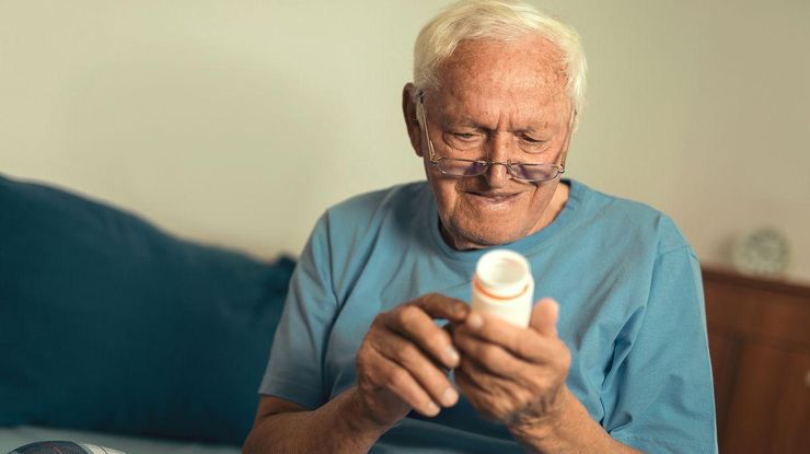 Older man at home reading a prescription medication label on his pill bottle