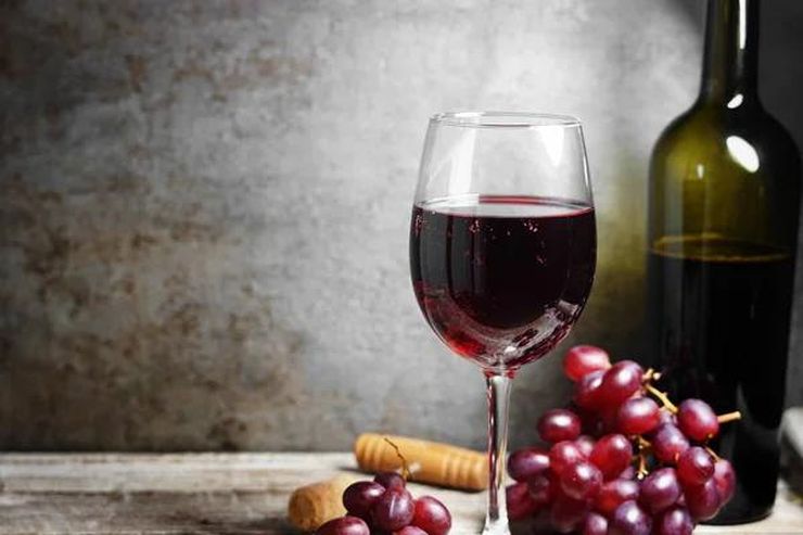 Glass of red wine with grapes and corks on a wooden table