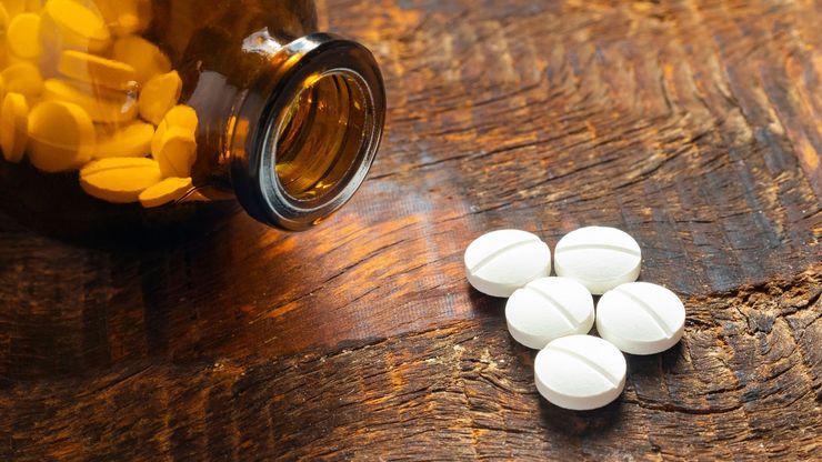 Close-up of white scored tablets with dividing lines next to an amber prescription bottle on a wooden table