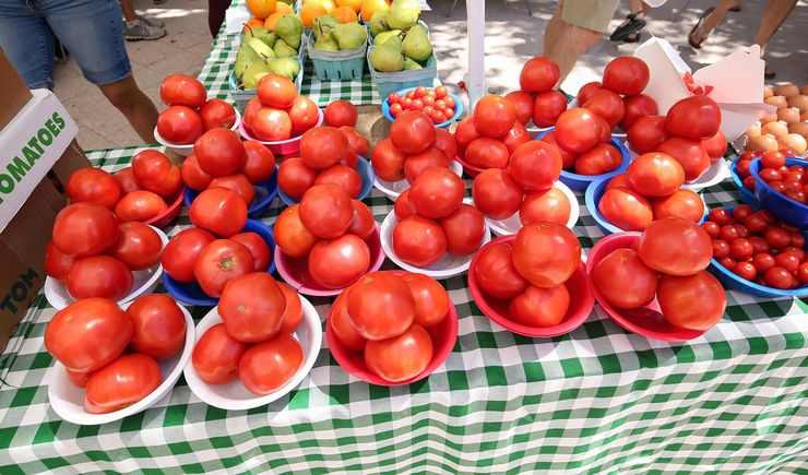 Fresh ripe tomatoes displayed in bowls at an outdoor farmers market stall
