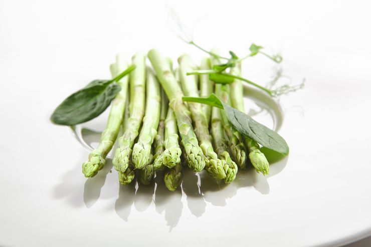 Fresh asparagus spears and spinach leaves on a white plate