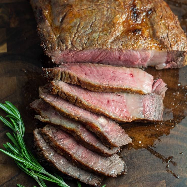 Cooked medium-rare beef steak sliced on a wooden cutting board, a low to moderate purine food when kept to a sensible portion