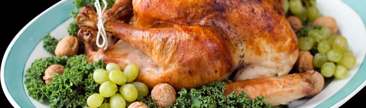 Whole roasted turkey on a platter with kale, grapes and walnuts