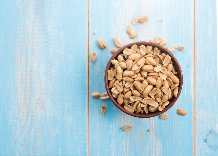 A small bowl of unsalted dry-roasted peanuts with a spoon on a kitchen table
