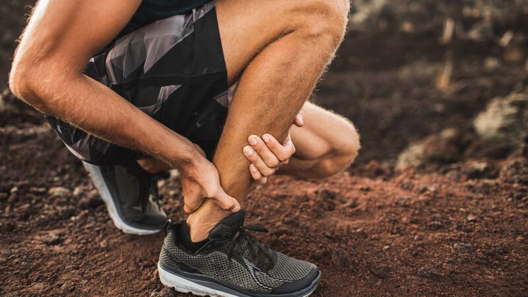 Runner stopping to hold a painful Achilles tendon at the back of the heel