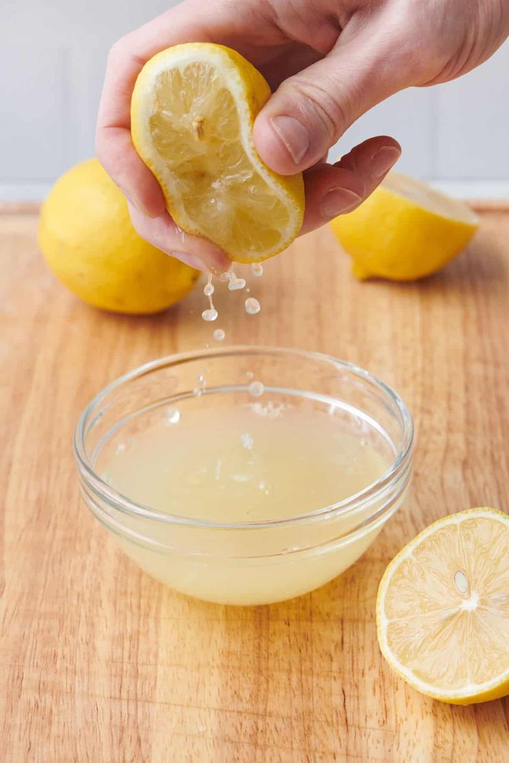 A hand squeezing fresh lemon juice into a glass bowl on a wooden cutting board