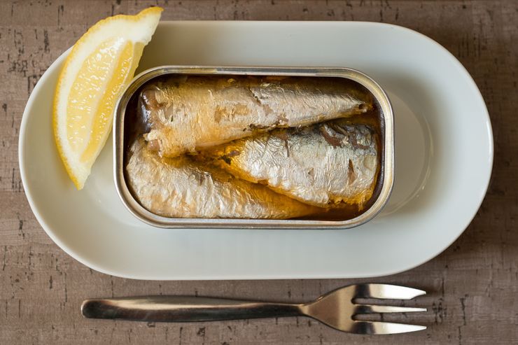 Open can of sardines on a plate with lemon and bread